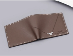 Detalle de cartera de cuero marrón con costuras blancas y adorno de greca plateado