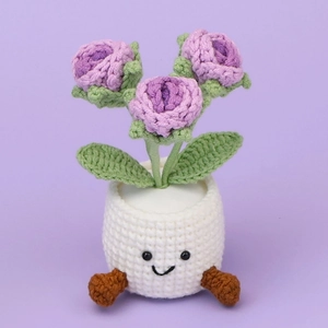 Detail of handmade crochet potted plant with purple flowers and smiling white pot
