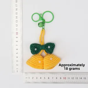 Detailed view of hand-knitted green and yellow bell pendant with dimensions on ruler