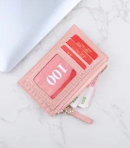 Détail d'un porte-cartes en cuir rose embossé crocodile avec zip doré et fenêtre d'identité