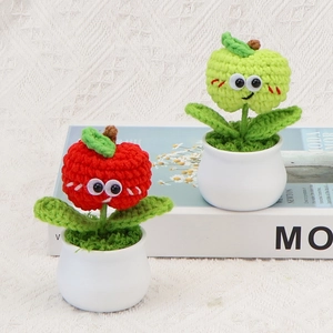Close-up of handmade crochet apple potted plants with cute faces and ceramic pots