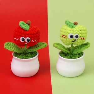 Close-up of handmade crochet apple potted plants with cartoon eyes and white ceramic pots