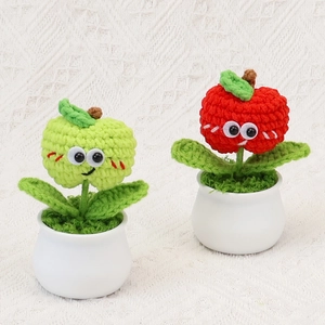 Macro shot of two handmade crochet apple plants in white pots with smiling faces
