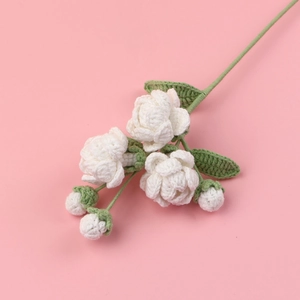 Handmade crochet jasmine flower stalk with white blossoms and green leaves on pink background