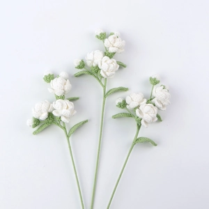 Macro detail of three handmade crochet jasmine flowers with clear knit textures and green leaves