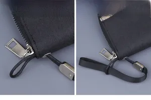 Detail of a black canvas clutch with silver zipper and detachable nylon wrist strap