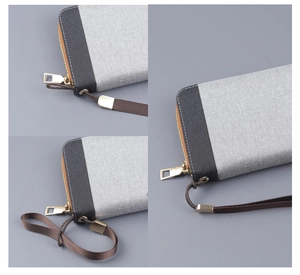 Detail of grey canvas clutch bag showing fine stitching and gold metal zipper with wrist strap