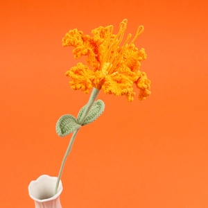 Handmade crochet orange lily flower in a white vase against a matching orange background