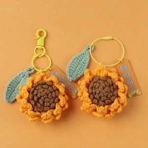 Handmade crochet sunflower keychain set with green leaf and yellow metal clasp on orange background