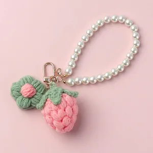Handmade crochet strawberry keychain with flower and pearl strap on pink background