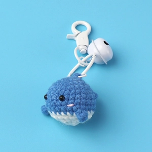 Handmade crochet blue whale keychain with white bell and lobster clasp on blue background