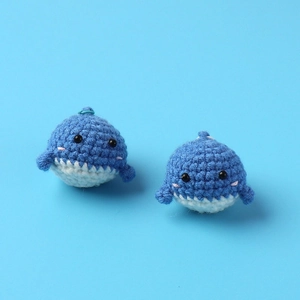 Close-up of handmade blue and white knitted whale keychain charms with pink blush details