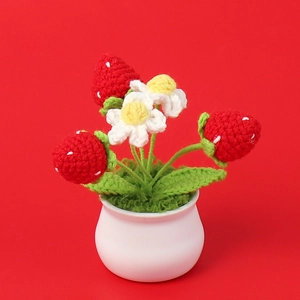 Detailed view of handmade crochet strawberry plant in a white ceramic pot on red background