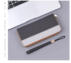 Detail of gray canvas men's long wallet with metallic zipper and wrist strap on desk