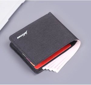 Detailed view of a slim black canvas bifold wallet with white logo on a gray desk surface