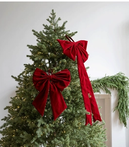Detail of oversized red velvet Christmas bows with long tails hanging on a lit tree