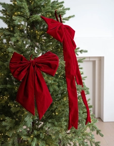Detail of red velvet Christmas bows with long streamers on a lit festive tree