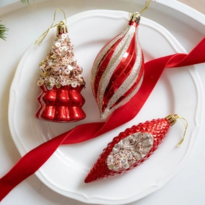 Red and gold Christmas tree ornaments in various shapes with glitter details on white plate