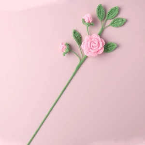 Dettaglio di una rosa rosa fatta a mano all'uncinetto con foglie verdi e piccoli boccioli