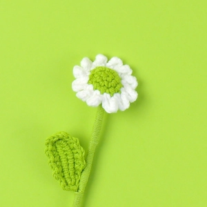 Detailed close-up of a handmade crochet daisy with white petals and green stem on green background