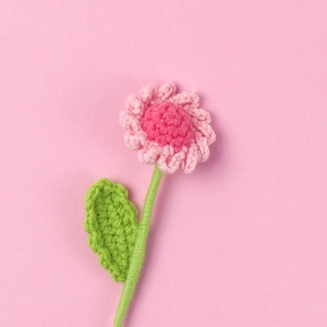 Macro view of handmade crochet pink daisy flower with green stem and leaf textures