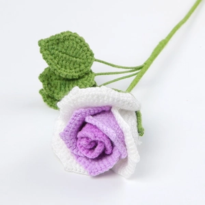 Detailed knit texture of a handmade white and purple crochet rose flower with green leaves