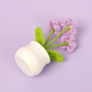 Detalle de planta de flores de ganchillo hechas a mano con base blanca sobre fondo morado