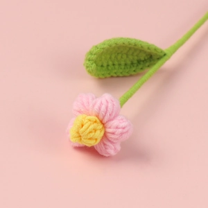 Vista macro di un fiore puff fatto a mano all'uncinetto con petali rosa e foglia