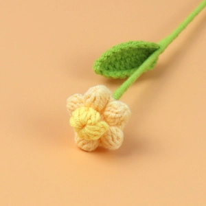 Macro di un fiore a sbuffo fatto a mano all'uncinetto arancione con stelo e foglia