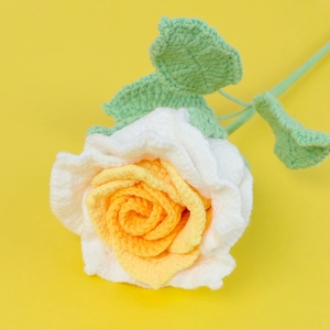 Close-up of handmade crochet rose with white petals and yellow center on stem
