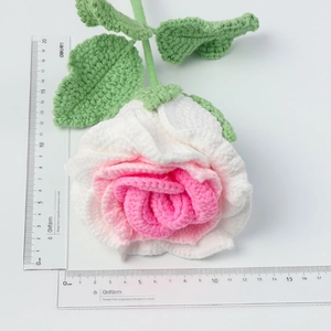 Handmade crochet rose with pink gradient petals and green leaves on white background