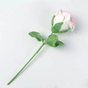 Detailed view of a handmade crochet rose with pink petals and green knitted leaves