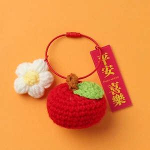 Macro detail of handmade crochet persimmon keyring with a peace and joy pendant