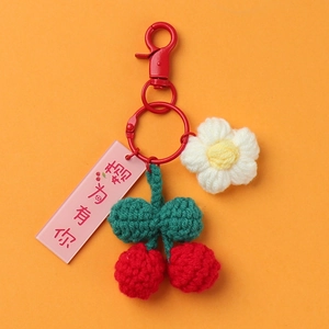 Macro detail of handmade crochet red cherry keychain with green leaves and a pink tag