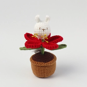 Close-up of handmade crochet rabbit flower in a pot with soft red petals and green leaves