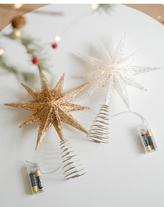 Close-up of lighted champagne and white star tree toppers with glitter and battery box