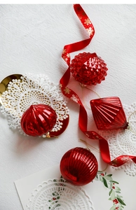 Macro shot of assorted red Christmas glass ornaments with gold ribbons on white lace