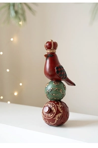 Close-up of a red resin bird with crown atop festive ornaments in holiday lighting