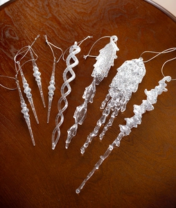 Close-up of seven clear acrylic icicle ornaments with glitter on a dark wood background