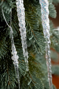 Detail of transparent glitter acrylic icicle ornaments hanging on a Christmas tree branch