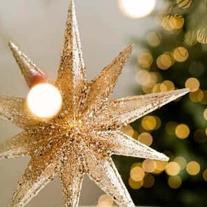 Sparkling champagne gold star tree topper with glitter finish on a festive tree