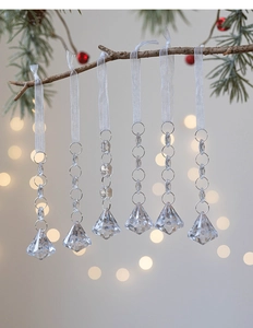 Detail of crystal acrylic ornaments hanging on pine branch with festive bokeh lights