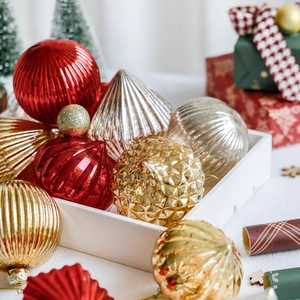Red and gold assorted glass Christmas ornaments in a white wooden tray display