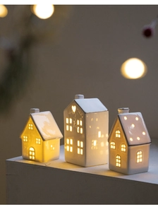 Close-up of three white ceramic glowing houses with gold roofs and heart cutouts