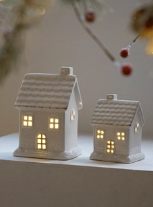 Detail view of two white ceramic light-up houses with gold trim and warm LED glow