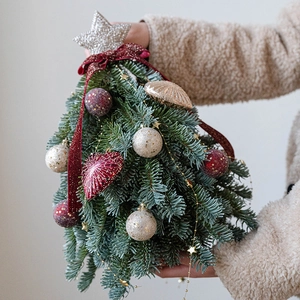 Mini árbol de Navidad de abeto noble con lazos rojos y estrella dorada en mano