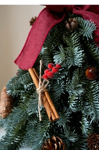 Detalle de mini árbol de Navidad artificial con palitos de canela y bayas rojas de adorno