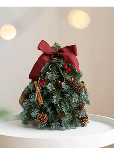 Detalle de mini árbol de Navidad con lazo rojo oscuro, piñas y palitos de canela