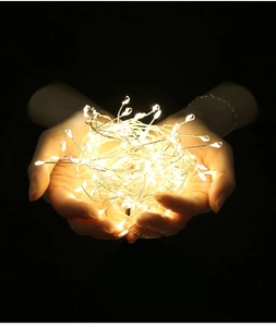 Gros plan de guirlandes LED en fil de cuivre blanc chaud tenues à la main sur fond noir