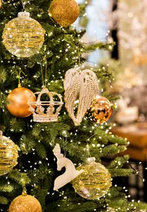 Detail of elegant gold and white Christmas ornaments hanging on a warm lit festive tree